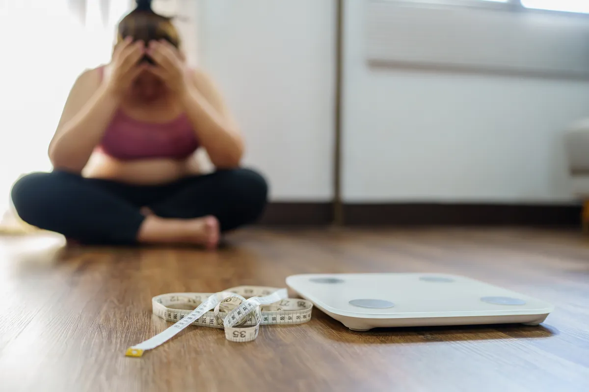 Žena zabrinuta pored vage – simbol neuspešnih dijeta i frustracije
